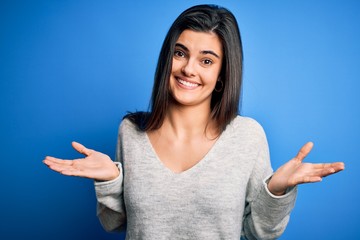 Young beautiful brunette woman wearing casual sweater standing over blue background clueless and...
