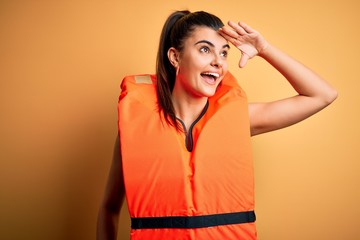Young beautiful brunette woman wearing orange safe lifejacket over yellow background very happy and...