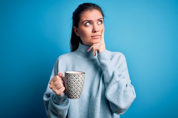 Young beautiful woman with blue eyes drinking mug of coffee over isolated background serious face...