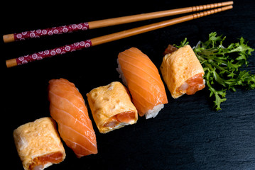 Japanese cuisines nigiri sushi set on black plate served with wasabi, soy sauce. Sushi Roll with salmon, sushi maki roll and tamago sushi on black plate