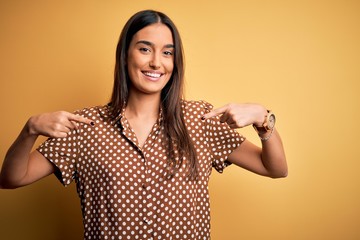 Young beautiful brunette woman wearing casual shirt over isolated yellow background looking confident with smile on face, pointing oneself with fingers proud and happy.