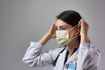 Woman healthcare professional demonstrating proper donning of mask for protection from coronavirus. Up close female healthcare worker putting on safety equipment on grey background