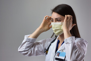 Woman healthcare professional demonstrating proper donning of mask for protection from coronavirus. Up close female healthcare worker putting on safety equipment on grey background