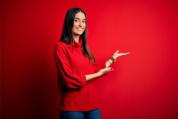 Young beautiful brunette woman wearing casual sweater over isolated red background Inviting to...