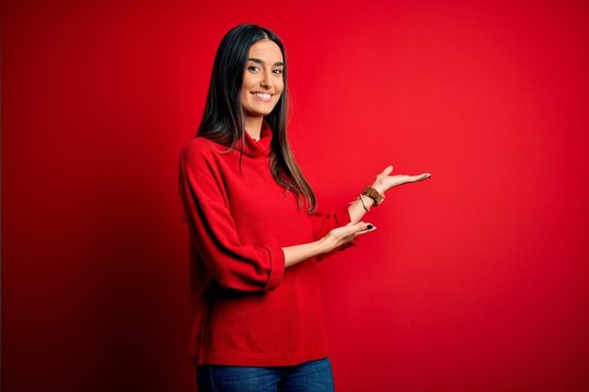 Young beautiful brunette woman wearing casual sweater over isolated red background Inviting to enter smiling natural with open hand