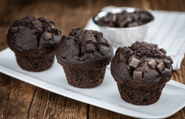 Old wooden table with fresh Chocolate Muffins (close-up shot; selective focus)