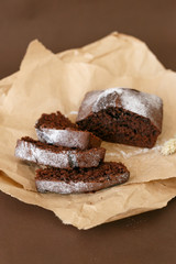Delicious sliced chocolate muffin. Chocolate muffin on dark parchment on a brown background. Chocolate muffin sprinkled with icing sugar.