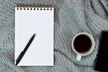 Flat-lay of Cosy working writing place with warm sweater coffee, note paper and smartphone. work from home. Writing.