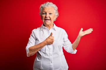 Senior beautiful woman wearing elegant shirt standing over isolated red background Showing palm hand and doing ok gesture with thumbs up, smiling happy and cheerful