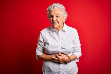 Senior beautiful woman wearing elegant shirt standing over isolated red background with hand on...