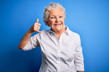 Senior beautiful woman wearing elegant shirt standing over isolated blue background smiling doing phone gesture with hand and fingers like talking on the telephone. Communicating concepts.