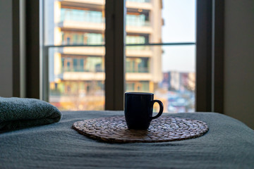 A cup of coffee of tea in bedroom in front of big window.