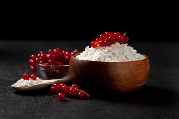 fresh home-made cottage cheese with currants in a wooden bowl against a dark background, healthy food with berries on a black table