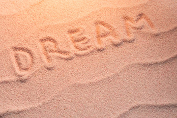 DREAM lettering on sand with wave and evening light. Minimal exotic vacation and travel concept, Flat lay top view copy space