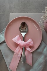 Festive table setting. Pink plate and cutlery with a pink bow on a gray background. Beautiful flat lay.