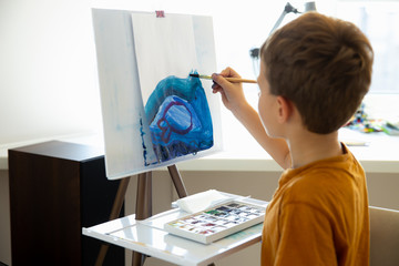 Cute little boy drawing with blue paints at home