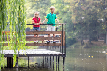 Two children boy and girl standing on wooden deck on a lake shore.