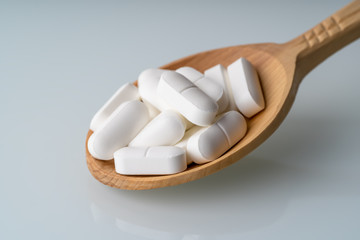 Fototapeta na wymiar Pharmaceutical medicine pills or white tablets or drugs on wooden spoon, macro photo.