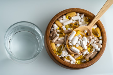 Top view of medicine pills, tablets and different drugs in wooden bowl with spoon and glass of water.