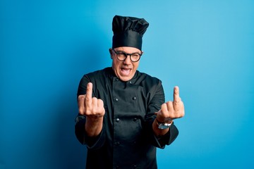 Middle age handsome grey-haired chef man wearing cooker uniform and hat Showing middle finger doing...