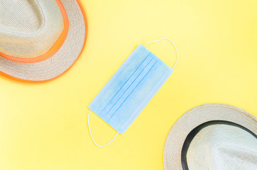Obraz premium Stay home, social distancing, summer vacation travel concept due to global pandemic coronavirus. Two straw hats separated by medical mask on yellow background. Flat lay, top view, copy space.
