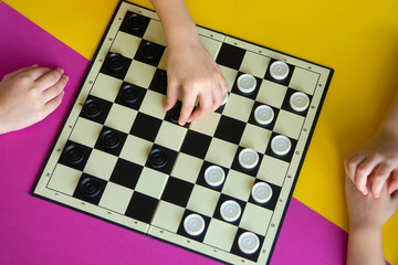 Children play checkers on a colorful table. Boy and a girl compete in board games. Top view.