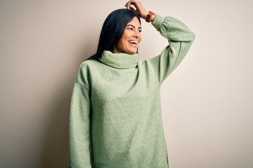 Young beautiful hispanic woman wearing green winter sweater over isolated background smiling confident touching hair with hand up gesture, posing attractive and fashionable