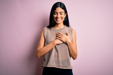 Obraz premium Young beautiful hispanic fashion woman wearing sweater over pink background smiling with hands on chest with closed eyes and grateful gesture on face. Health concept.