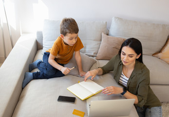 Beautiful young woman helping son to do homework online