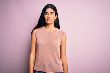 Obraz premium Young beautiful hispanic fashion woman wearing casual sweater over pink background with serious expression on face. Simple and natural looking at the camera.