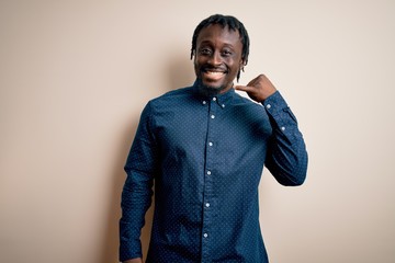 Young handsome african american man wearing casual shirt standing over white background smiling doing phone gesture with hand and fingers like talking on the telephone. Communicating concepts.