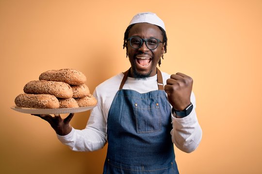 Young african american bakery man holding tray with healthy wholemeal bread screaming proud and celebrating victory and success very excited, cheering emotion