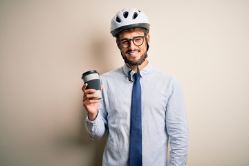 Naklejka premium Young businessman wearing glasses and bike helmet drinking cup of coffee with a happy face standing and smiling with a confident smile showing teeth