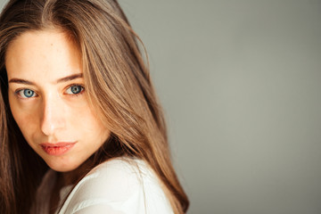 Serious girl with her hair in bright clothes on a gray background, close-up. Nude makeup, without...