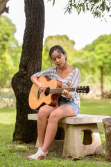 Full body shot of young Asian woman playing guitar at the park