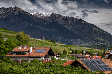 Panorama of solar batteries on roof top, green slopes of the mountains of Italy, Trentino, Dolomites, huge clouds over a valley, green meadows, a clear energy, energy of the sun, Solar panels