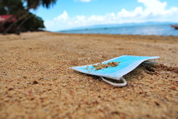 Fototapeta na wymiar A medical mask is lying on a sandy tropical beach against the background of the sea