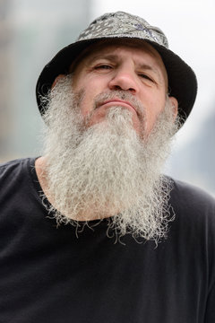 Face of mature bearded man with hat against view of the city