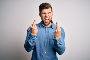 Young handsome blond man with beard and blue eyes wearing casual denim shirt Showing middle finger...