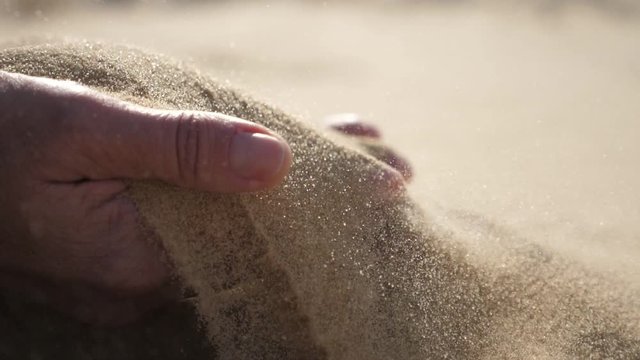 Two hands raising hot sand up and streaming it down in a desert in sunny spring