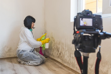 Video camera filming how woman cleaning mold from wall using spray bottle with mildew removal products.
