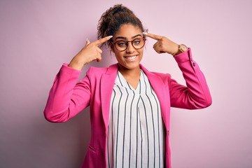 Beautiful african american businesswoman wearing jacket and glasses over pink background smiling pointing to head with both hands finger, great idea or thought, good memory