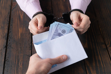men's hands give money in envelope to women's hands in handcuffs against the background of a wooden table
