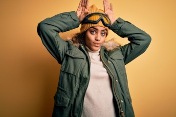Young african american afro skier girl wearing snow sportswear and ski goggles Doing bunny ears...