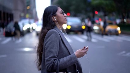 Slow motion effect of young executive manager in formal apparel happy from listening music songs via cellphone application and modern electronic earphones, Indian person crossing road in downtown
