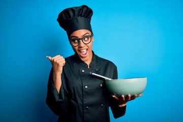 Young african american chef girl wearing cooker uniform and hat using whisk and bowl pointing and...