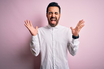 Young handsome man with beard wearing casual shirt standing over pink background celebrating mad...