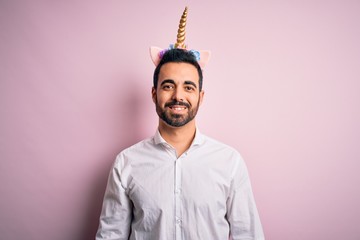 Young handsome man with beard wearing funny unicorn diadem over pink background with a happy and cool smile on face. Lucky person. © Krakenimages.com