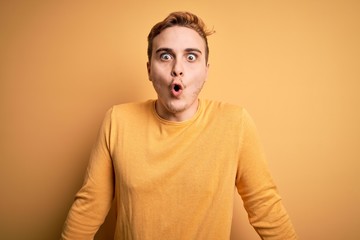 Young handsome redhead man wearing casual sweater over isolated yellow background afraid and shocked with surprise expression, fear and excited face.