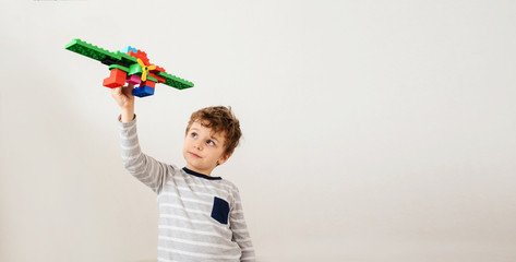Little boy is playing with a toy plane built of plastic bricks